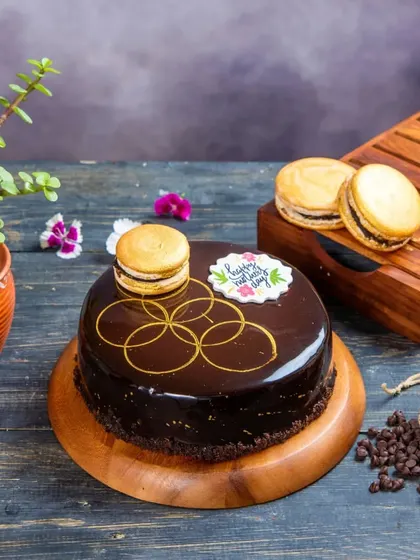 An elegant Dark Chocolate Fantasy cake, decorated with a golden macaron and a beautiful hand-drawn pattern. This premium cake is perfect for special occasions like Mother's Day.