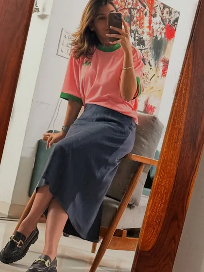 A trendy look with a pink t-shirt, midi skirt, and loafers, showing a more playful and modern style.