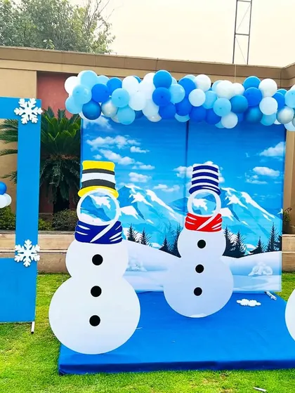 A fun winter-themed outdoor setup. This decoration includes a snowy mountain backdrop, snowman cutouts, and a photo frame, perfect for a seasonal party.
