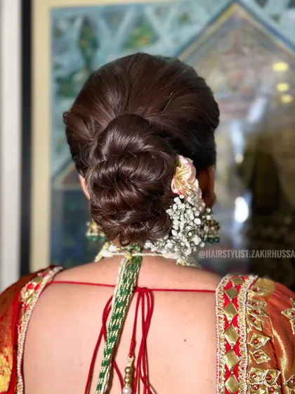 I crafted this traditional bridal bun for a client wearing a classic red and gold saree. The updo is decorated with a mix of fresh carnations and baby's breath for a fragrant and beautiful finish.