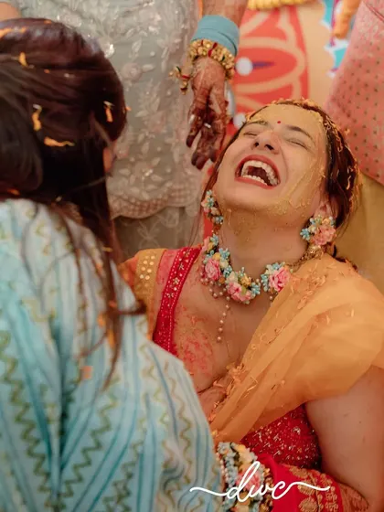 A candid shot of pure joy during a Haldi ceremony, with the bride bursting into laughter as she's covered in turmeric by her loved ones.