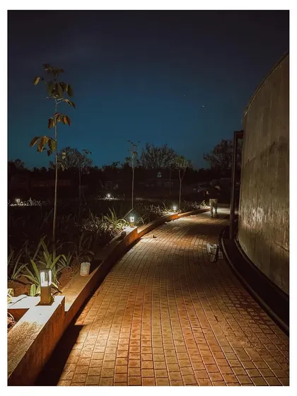 An evening view along the curved pathway of the memorial complex. The subtle landscape lighting illuminates the walkway and highlights the texture of the brick pavers, creating a safe and serene atmosphere after sunset.