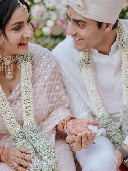 A sweet moment during the ceremony where the groom holds a small object in the bride's henna-covered hand.