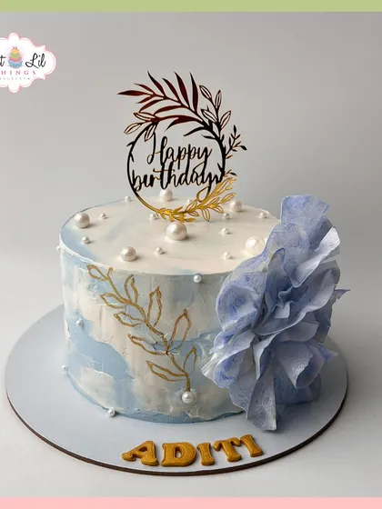 A beautiful birthday cake for Aditi, with a blue watercolor effect, hand-painted gold leaves, and a delicate wafer paper flower.