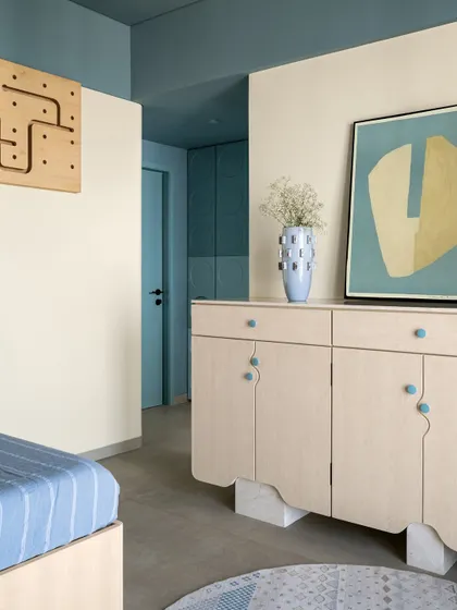 A view of the son's room, showing the custom credenza with its wavy base and playful blue knobs, continuing the theme of soft geometry and color.