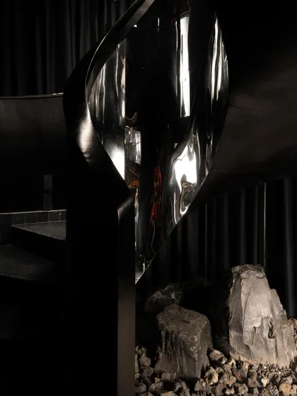 The sculptural spiral staircase at Lair, wrapped in a distorted, reflective metal. It is not just for circulation but is a centerpiece that fragments and abstracts the surrounding darkness.