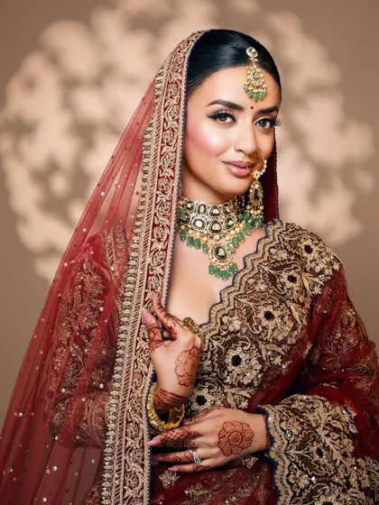 A classic bridal pose under a sheer dupatta, highlighting the rich maroon tones and detailed embroidery of the lehenga.