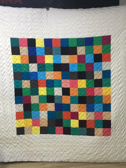 A minimalist modern quilt featuring a grid of colorful squares against a clean white background with a chevron-quilted border.
