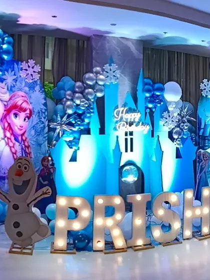 Bringing the magic of Arendelle to life with a complete Frozen theme party setup. This includes character cutouts of Elsa, Anna, and Olaf, an illuminated ice castle backdrop, snowflake details, and a balloon garland in signature icy blue, white, and silver tones. The light-up marquee letters for the name make it extra special.