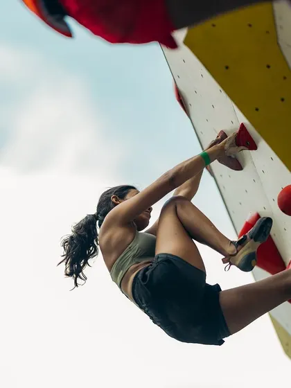 A low angle shot capturing a climber's powerful movement and precision. The chalk on her hands is essential for grip, especially in the humid festival environment.