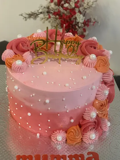 A beautiful pink and orange ombre cake. The side is decorated with a cascade of buttercream rosettes and pearls.