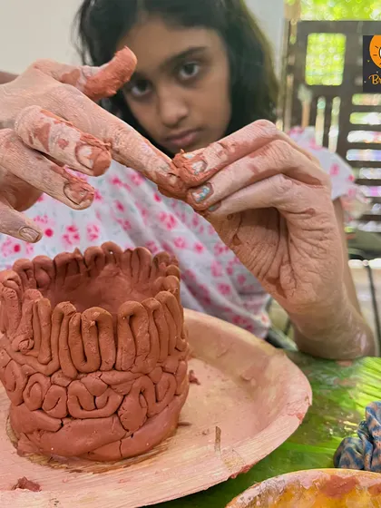 The intense focus of a young artist creating her coiled clay pot. You can see her carefully shaping and attaching the coils, completely absorbed in the creative process.