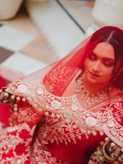 A high-angle shot of the bride looking down, her red veil creating a beautiful pattern over her. This artistic portrait highlights the delicate details of her attire.