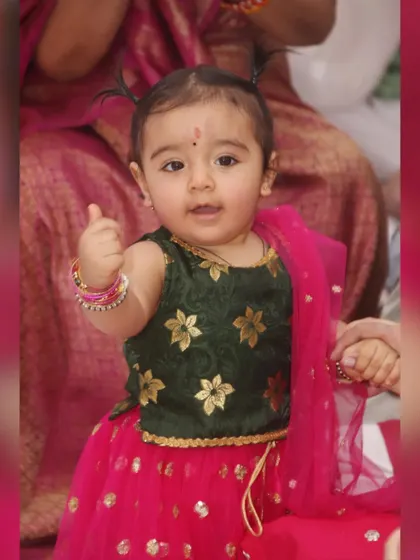 An adorable baby girl in a traditional lehenga gives a thumbs-up to the camera. We love capturing these cute and spontaneous gestures.