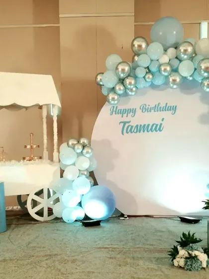 For a modern and elegant birthday, I created this pastel blue and silver chrome setup for Tasmai. The design includes a clean, circular white backdrop for personalized messaging, a stylish dessert cart, and a sophisticated balloon half-arch.