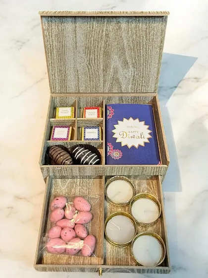 This elegant wooden box with a pull-out drawer is a premium corporate gift. The top compartment holds assorted chocolates and a Diwali card, while the drawer reveals scented candles and strawberry-coated almonds.