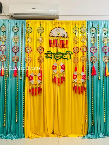 A unique Mehendi backdrop with blue and yellow drapes and a variety of traditional and bohemian-style hangings.