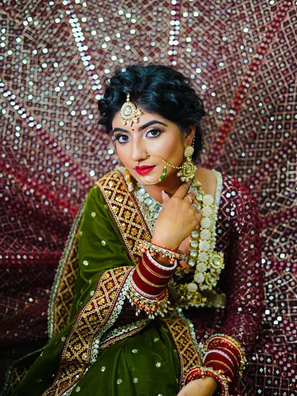 A beautiful bridal portrait against a shimmering backdrop. The combination of a green velvet blouse and a deep red dupatta is perfectly complemented by the traditional jewellery and bold makeup.