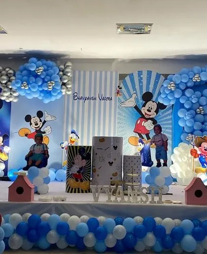 An elaborate Mickey Mouse themed birthday party stage, filled with blue and white balloons, character cutouts, and personalized backdrops.