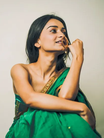 A bold and artistic portrait of a woman in a green saree, worn in a modern, strapless style, highlighting her smile and traditional nath.