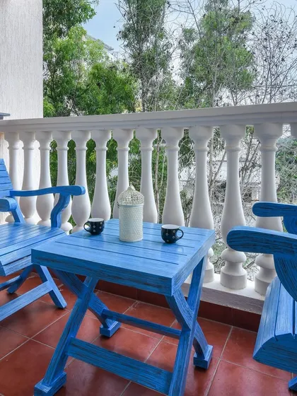 A charming balcony setup with bright blue foldable wooden chairs and a matching table. We help you create small outdoor retreats like this, perfect for enjoying a morning cup of tea.