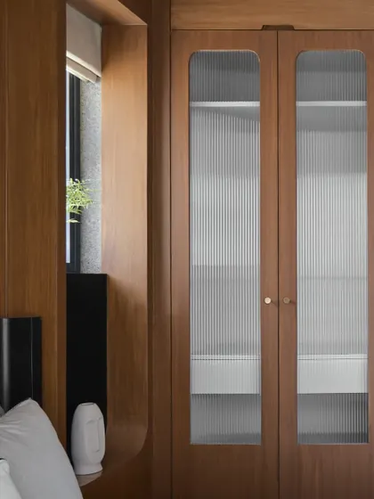 A closer view of the fluted glass wardrobe, which morphs into a wall unit that frames a window. This innovative solution is a great example of the Japandi ethos of functional, beautiful design.