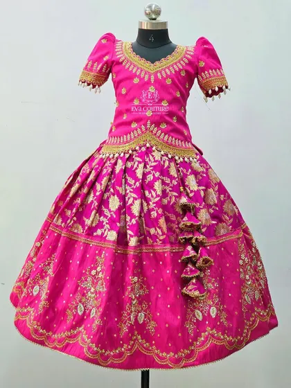 A close-up of a pink Banarasi silk lehenga. This shows the heavy maggam work that details the blouse and runs along the border of the skirt, making it perfect for weddings.