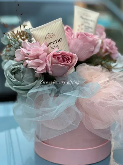 A close-up of a beautiful floral arrangement in a pink hat box, cleverly incorporating Aveeno baby lotion. It's a perfect gift that combines beauty for mom and practicality for baby.