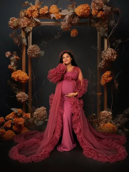 A moody and artistic solo portrait in a dusty rose ruffled gown. The mom-to-be is framed by an ornate arch decorated with autumn-toned florals.