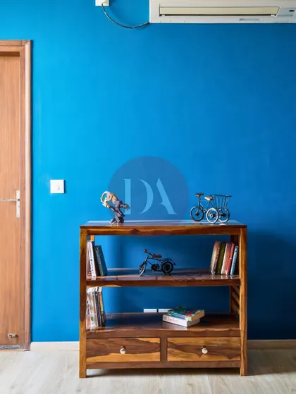 A close-up of the wooden bookshelf and decor against the blue wall. The small decorative pieces, like the miniature bicycle, add a touch of personal charm to the room.