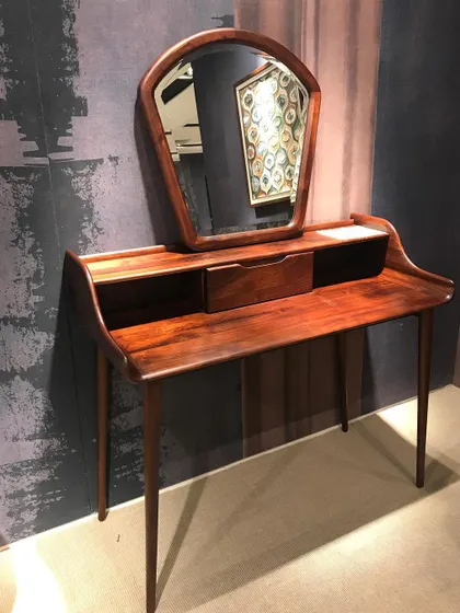 This custom-made dressing table, or console table, is crafted from solid wood with a vintage-inspired design. It features a uniquely shaped mirror, a small drawer for essentials, and slender, tapered legs, making it a charming and functional addition to a bedroom.