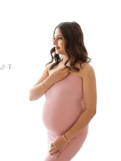 A minimalist and chic portrait. The mom-to-be wears a simple pink bodycon dress, her elegant pose highlighting the beauty of her pregnancy.