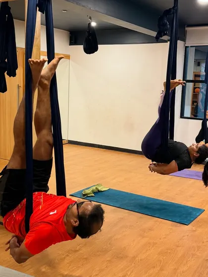 A father and daughter enjoy an inverted pose together. Aerial yoga is a fantastic way for families to bond, laugh, and try something new.