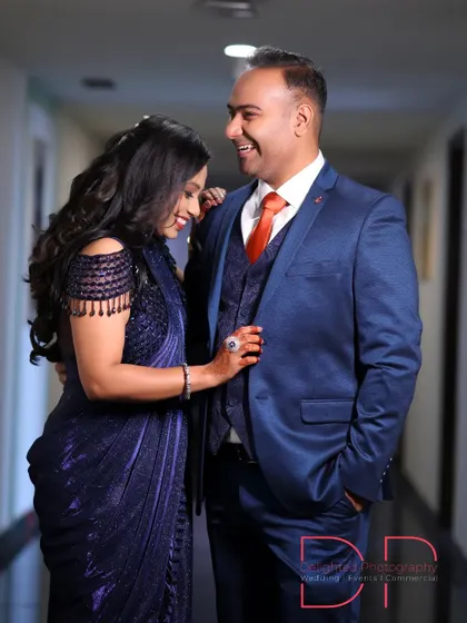 A candid shot of a couple sharing a laugh during their event. The woman's stylish navy blue saree and the man's coordinating suit are perfectly captured.
