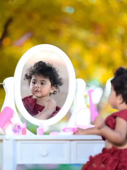 A little girl playing with makeup props in a beautiful outdoor setting, looking at her reflection in the mirror.