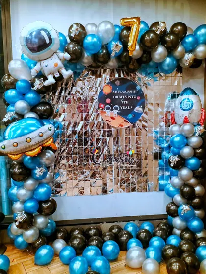 An out-of-this-world Space theme for a 7th birthday, with a silver shimmer backdrop, planet-themed banner, and astronaut and rocket ship balloons.
