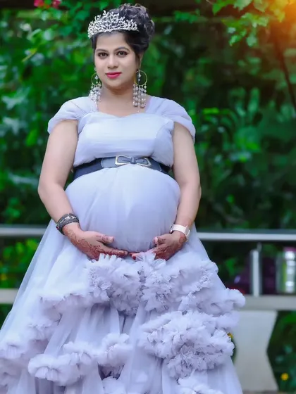 A beautiful solo maternity portrait of a woman in a grey ruffled gown with a tiara, posing in a garden.