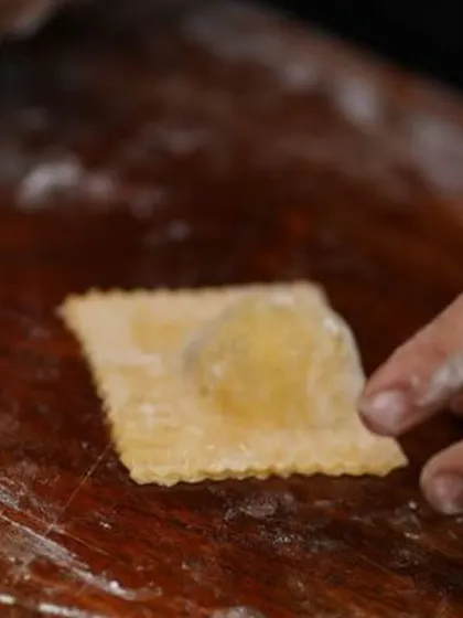 A single, perfectly formed raviolo before being cooked. This image highlights the delicate process of creating stuffed pasta, a specialty at our exclusive sit-down catering events.