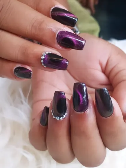 A deep purple cat-eye effect on coffin nails. This design is enhanced with a cluster of rhinestones at the cuticle for an extra touch of glamour.