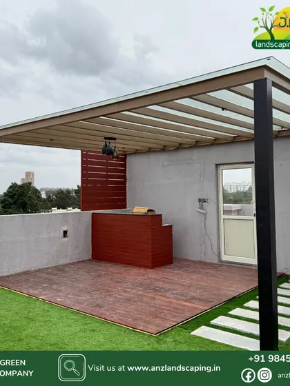 This modern terrace design combines multiple elements for a functional and beautiful space. It features a glass-roof pergola over a wooden deck with a custom bar counter, bordered by low-maintenance artificial grass and stone pavers.