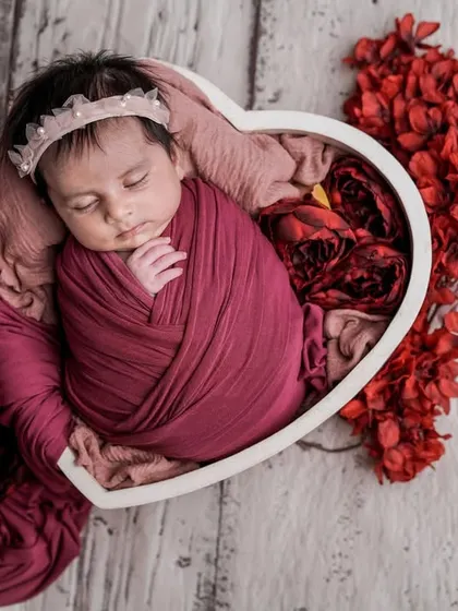 A heart full of love. This swaddled baby, nestled in a heart-shaped bowl with red flowers, is the perfect picture of romance and new life.