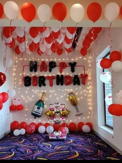 A full room decoration in red and white, with a "Happy Birthday" banner, champagne foil balloons, and a gift box centerpiece.