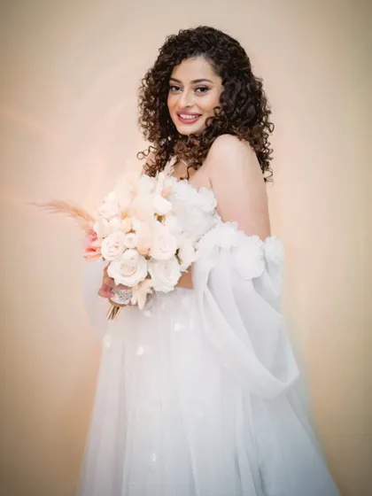 This bride's smile is absolutely radiant. Her off-the-shoulder gown and curly hairstyle create a look that is both modern and romantic.