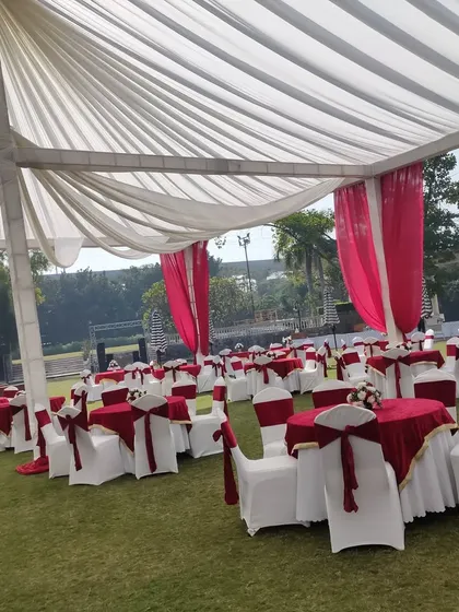 This image shows a classic banquet seating arrangement on a lawn, perfect for a wedding lunch. The tables are dressed in red and white linen, matching the drapes of the tent structure.