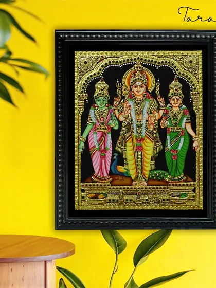 A stunning Tanjore painting of Lord Murugan with his consorts Valli and Devayani. The vibrant green of the deities against the black background creates a striking visual, highlighted by the intricate gold work.