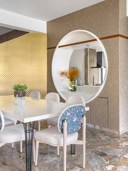 A whimsical touch in this Mumbai apartment, where a circular partition with a hidden Corian wash basin separates the dining area. The floral-patterned chair and bold gold backdrop add a layer of playful sophistication.
