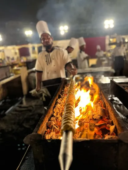 A chef manages a flaming grill, expertly cooking seekh kebabs for guests.