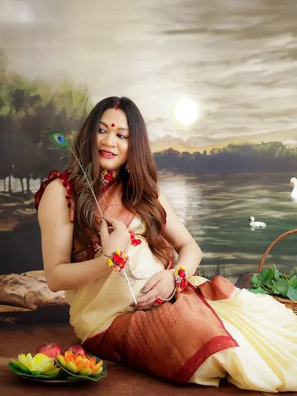 A beautiful traditional Bengali maternity portrait. The mom-to-be is dressed in a classic saree, holding a peacock feather against a painted backdrop.