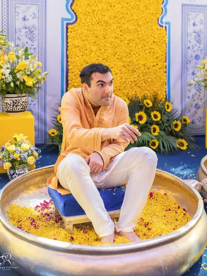 The groom's playful expression as he sits in a pot of flowers, waiting for the Haldi to begin.