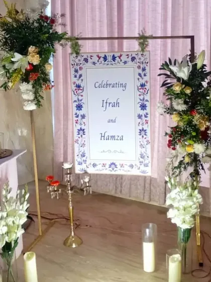 A welcome sign for Ifrah and Hamza's celebration, framed by two large, beautiful floral arrangements on pedestals.